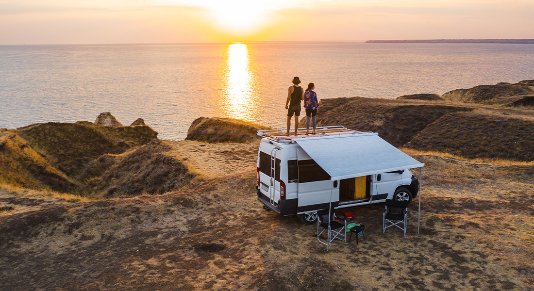 Two people Standing on Top of Class B Motorhome Overlooking Sunset on The Ocean